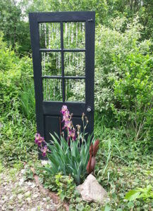 alt="old door in garden with hanging prisms in place of the windows"